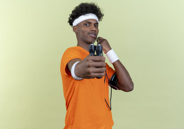 穿看着镜头年轻的美国黑人运动男子戴着头带和腕带举着跳绳镜头隔离在绿色的背景头带绳子运动