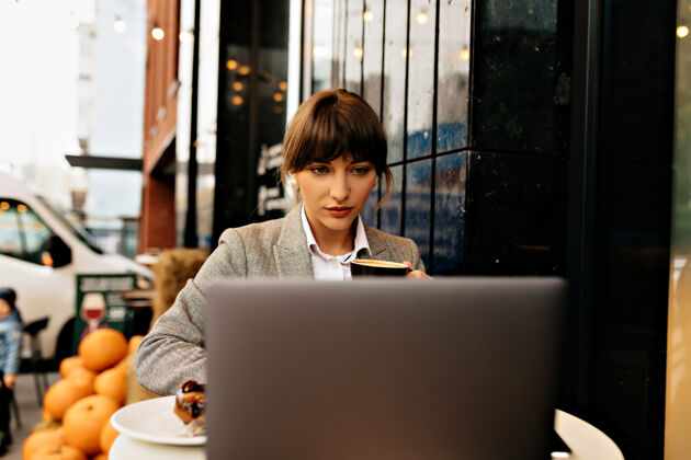 女士自信的女商人在街边咖啡馆用笔记本电脑工作 在键盘上打字 聪明的女士认真地看着屏幕商业女性工作魅力