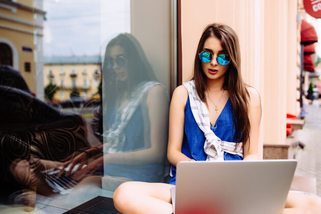 咖啡美丽的年轻女子坐在夏日的肖像 而使用笔记本电脑和无线耳机的视频通话人笔记本电脑女孩