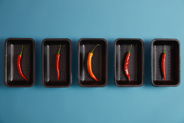 开销各种红辣椒和一个橙色辣椒 包装在黑色托盘在市场上 隔离在蓝色背景上 可以作为香料添加到您的菜热产品调味品和烹饪概念胡椒美食热