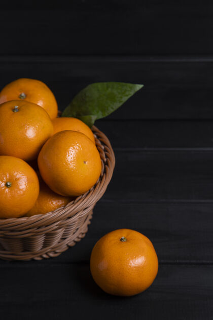 成熟的一个柳条篮子装满了新鲜的橘子和叶子放在一张深色的木桌上高质量的照片收获有机自然