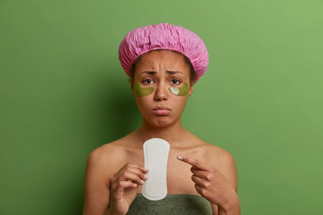 月照片中不高兴闷闷不乐的女人指着干净的卫生巾 有经期抽筋 月经期间心情不好 戴眼罩 淋浴帽女人 卫生 妇科 身体护理的概念站吸收洗澡
