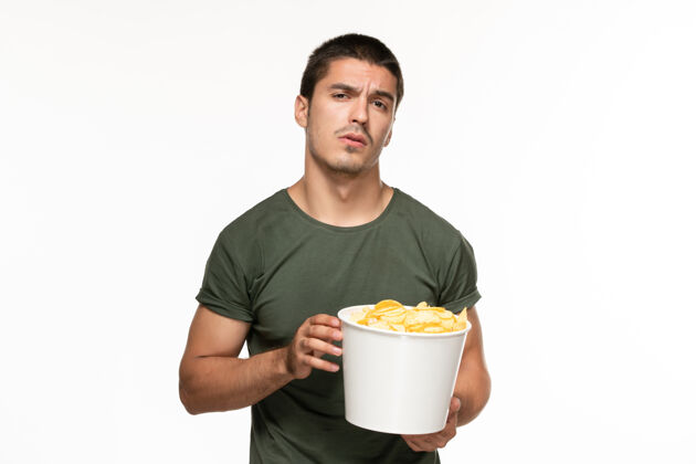 成人正面图身穿绿色t恤的年轻男子拿着篮子和土豆在白色的墙上孤独地享受电影土豆杯子电影