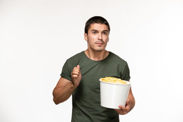 土豆正面图身穿绿色t恤的年轻男性手持土豆cips站在浅白的墙上孤独的人灯光电影杯子