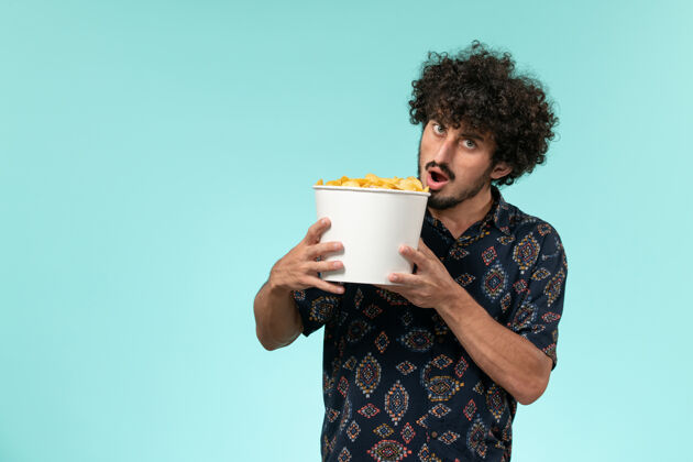 肖像前视图年轻人拿着篮子和土豆在蓝色墙上cips男性电影遥控器视图电影电影