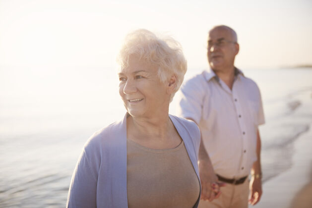 照明老年夫妇在沙滩 退休和暑假的概念爱人欢乐快乐