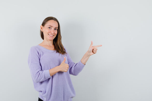 漂亮一位年轻的女性 穿着淡紫色的衬衫 一边指着一边 一边向上竖起大拇指 正面看去卷曲自信女士