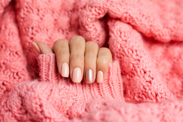 时尚漂亮的裸色美甲 一个手指闪亮的金色 在针织粉色羊毛枕头的背景下健康上光油美容师