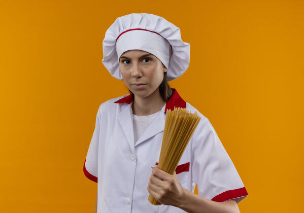 意大利面穿着厨师制服的年轻自信的白人厨师女孩拿着一束橙色的意大利面 留有复印空间空间复制橙色