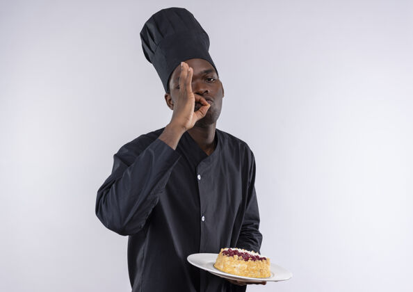 盘子年轻的美籍黑人厨师身着厨师制服 拿着盘子上的蛋糕 在白色的空白处摆出美味的手势年轻烹饪空间