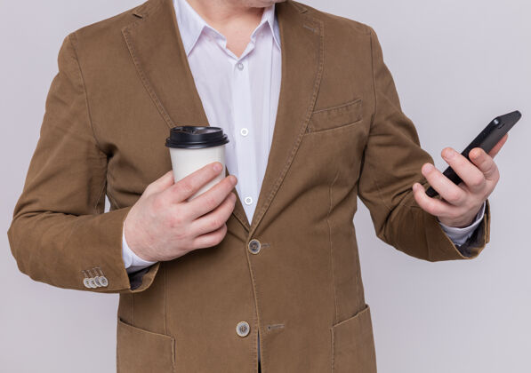 纸一个穿着西装的男人拿着手机和纸杯站在白色的墙上拿着男人杯子