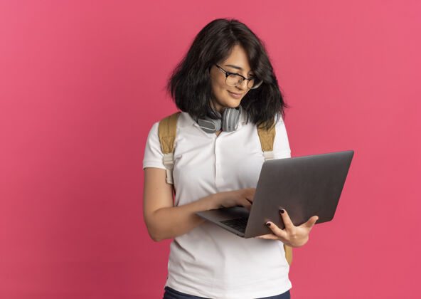 漂亮年轻漂亮的高加索女学生戴着耳机戴着眼镜背着书包拿着粉色的笔记本电脑 还有复印空间请脖子耳机