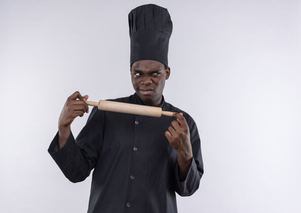 空间年轻恼怒的非洲裔美国厨师穿着厨师制服拿着擀面杖 看着白色的一面 留着复印空间别针年轻非裔美国人