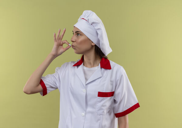 制服年轻自信的白种人厨师女孩穿着厨师制服 在绿色的空间里做着美味的手势空间厨师复制