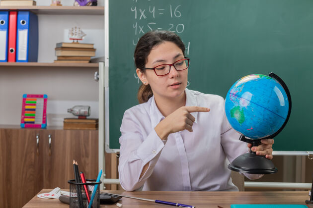 课戴眼镜的年轻女老师拿着地球仪讲课解释学校眼镜