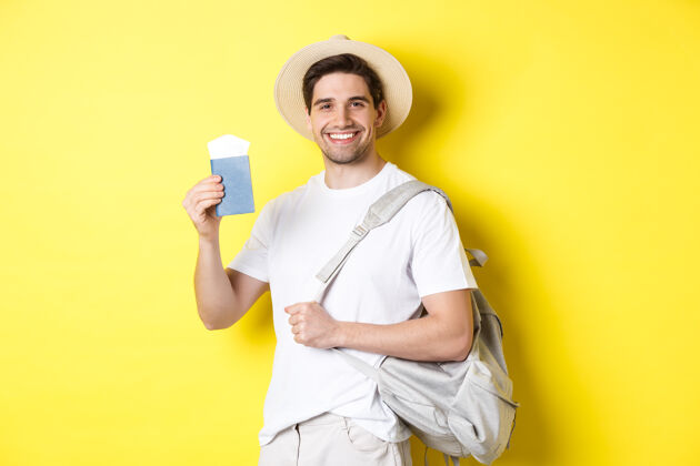 假日旅游度假带着微笑的年轻人去旅行 背着背包 拿着机票出示护照 站在黄色的背景上背包护照夏天