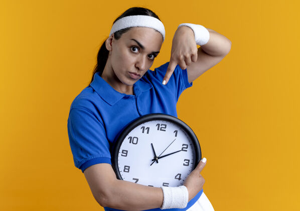 复制年轻自信的白人运动女性戴着头带和腕带拿着并指着橙色的时钟 留着复制空间头带年轻信心