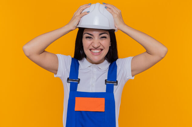 年轻人身穿施工制服 头戴安全帽的年轻建筑工人站在橙色的墙上 手举头看着前面 脸上带着恼怒的表情制服建筑头