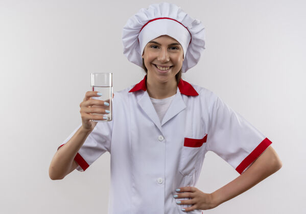 玻璃身着厨师制服 面带微笑的白人年轻厨师女孩手持一杯水 将手放在白色的腰部 留有复制空间年轻腰持有