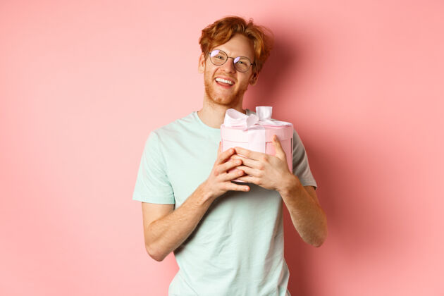 眼镜情人节和浪漫的概念快乐的红发男朋友收到浪漫的礼物 拥抱盒子和礼物说谢谢 微笑着感激 粉红色背景感激人脸