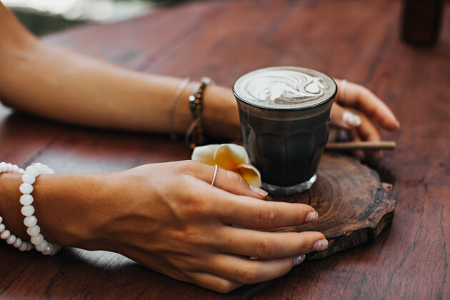 马克杯晒黑的女性双手捧着一杯椰子奶咖啡热美丽木头
