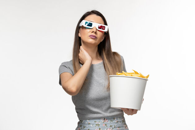 抱着的正面图年轻女性手持芯片 戴着d型太阳镜在白色表面上看电影漂亮的电影眼镜
