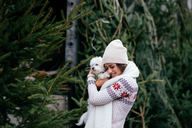 小市场上一棵绿色的圣诞树旁 一个抱着一只白色狗的女人肖像圣诞微笑