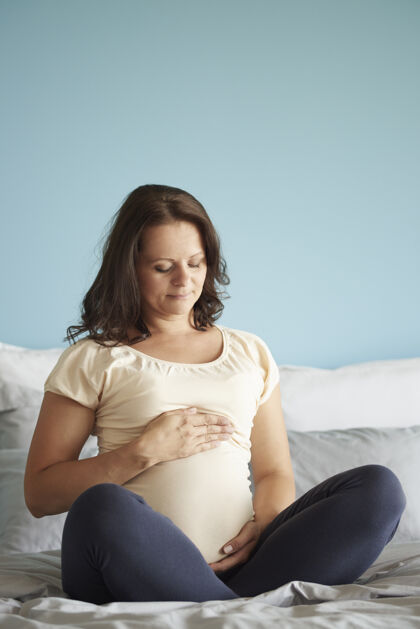 后代盘腿坐在床上的未来母亲怀孕中风期望