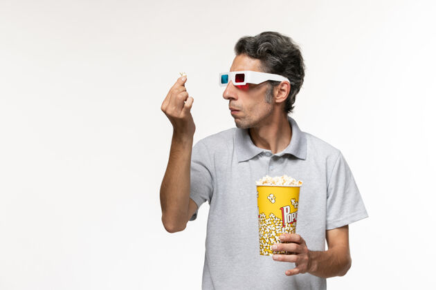 探索正面图：年轻男性手持爆米花 戴着d型太阳镜 在白色表面探索玉米电影院爆米花衬衫