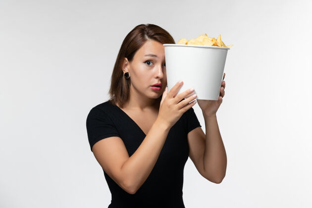 漂亮正面图：年轻女性手持薯片 在白色表面上看电影电影院年轻女性土豆
