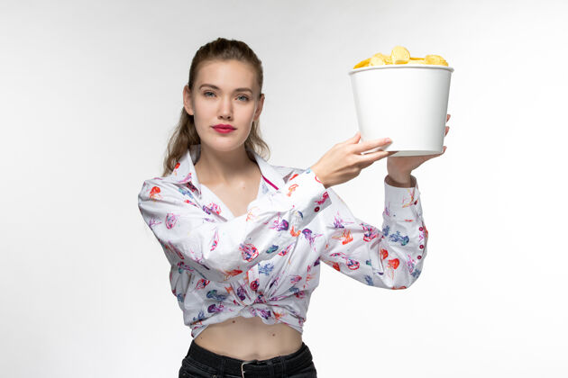 漂亮正面图：年轻的女性拿着篮子 拿着薯片 在白色的表面上看电影抱着年轻女性电影院