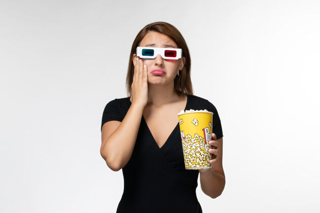抱正面图戴着d型太阳镜拿着爆米花看电影的年轻女性在白色的表面哭泣性感孤独太阳镜