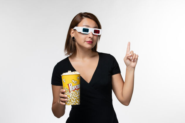 年轻女性正面图戴着d型太阳镜拿着爆米花的年轻女性在白色表面上看电影前面太阳镜电影