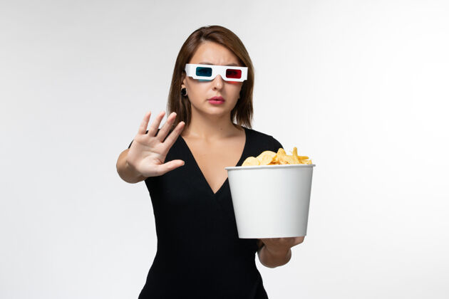 孤独正面图：年轻女性戴着d型太阳镜拿着薯片 在白色表面上看电影太阳镜看漂亮
