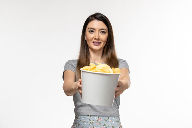 前面正面图：年轻的女性拿着土豆片篮子 微笑着站在白色的表面上电影院遥远土豆