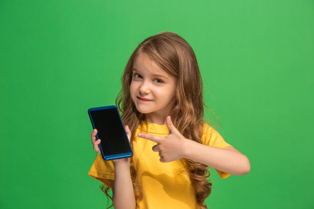 站立快乐的少女站在时尚的绿色工作室墙上 用手机微笑着脸年轻微笑
