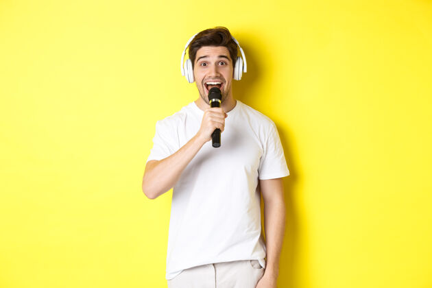 黄色戴着耳机拿着麦克风 唱着卡拉OK歌 穿着白衣服站在黄色背景上男人录音室成人