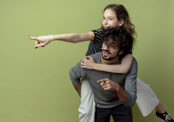 手指一对年轻的男女在一起玩得很开心 男人背着他的女朋友 而女人则用手指着绿墙上的东西年轻而在一起