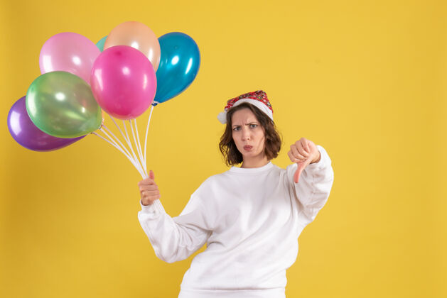 吹正面图年轻漂亮的女子手持五颜六色的气球对黄色的情感圣诞新年女人的颜色庆祝气球颜色