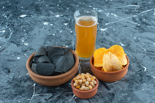 新鲜各种各样的开胃菜在碗里和一杯啤酒 在蓝色的背景上啤酒碗黑薯条