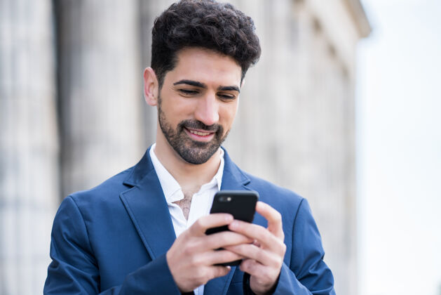 男性一个商人站在街上使用手机的肖像商业和城市概念正面应用程序城市