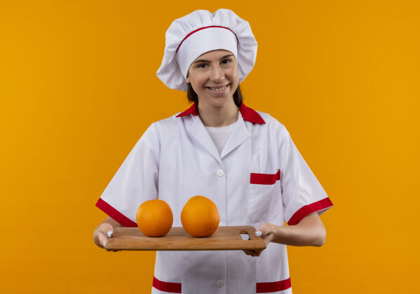 持有身着厨师制服 面带微笑的白人年轻厨师女孩将橘子放在砧板上 橘子空间与复印空间隔离开来年轻女孩橙色