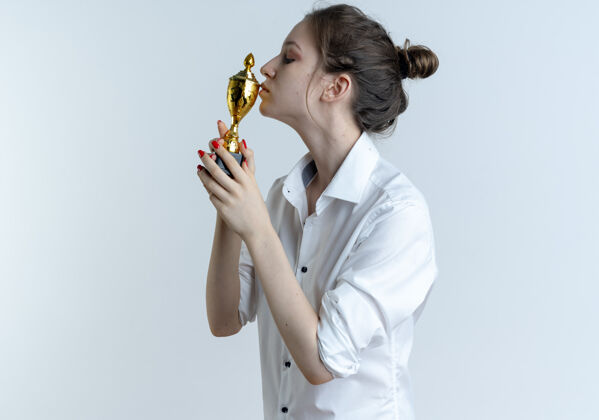 金发年轻自信的金发俄罗斯女孩拿着和亲吻冠军杯隔离在白色空间与复制空间杯复制举行