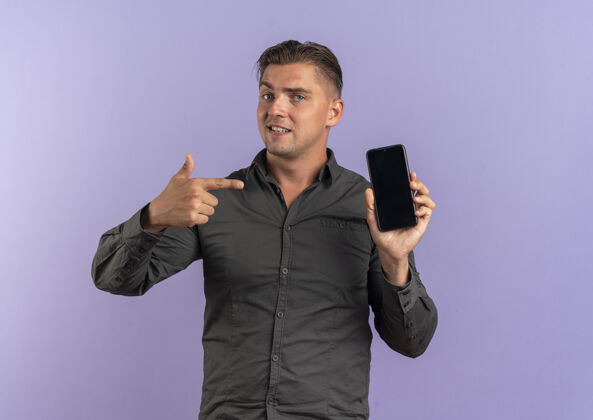 英俊年轻自信的金发帅哥拿着手机指着紫罗兰色的空间和复印空间点持有男人
