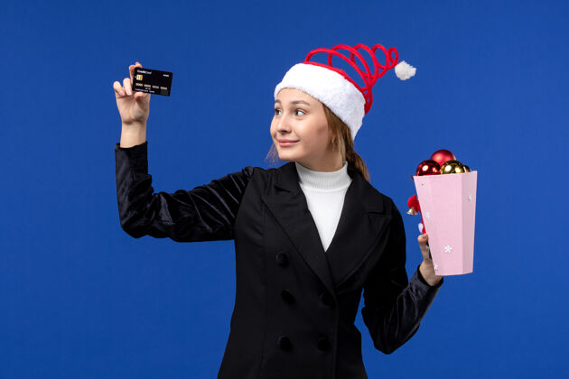 银行正面图：带着圣诞树玩具和银行卡的年轻女士在蓝色的墙壁上欢度新年人玩具微笑