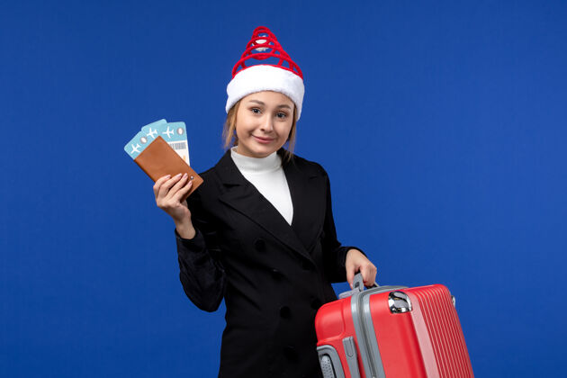 圣诞节正面图：年轻女子拿着蓝色背景女子度假包的票人成人人