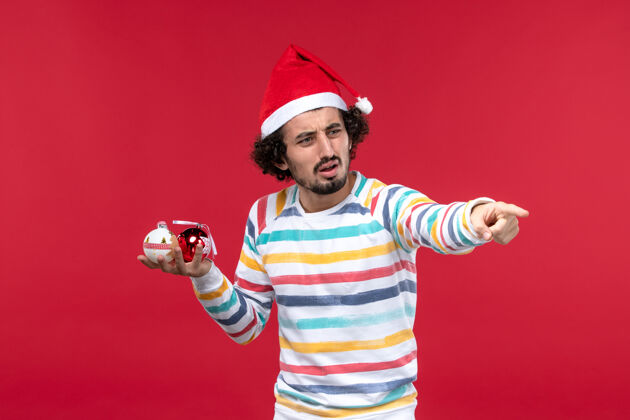 人正面图年轻人手持圣诞树玩具红墙新年人类节日红年轻人视图人