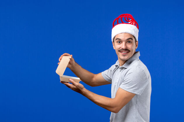 圣诞节正面图年轻男性拿着食物包在蓝色的墙上男性的食物服务工作前面工作肖像