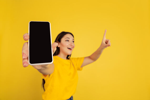 黑发显示空白手机屏幕黄色工作室背景上孤立的白种女人肖像休闲的漂亮深色模特人类情感的概念 面部表情 销售 广告 复制空间工作半帅气