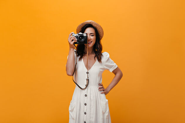 复古相机穿着时髦夏装的漂亮女孩在复古相机上拍照穿着白色长裙戴着帽子的时髦女人微笑着室内衬衫情感